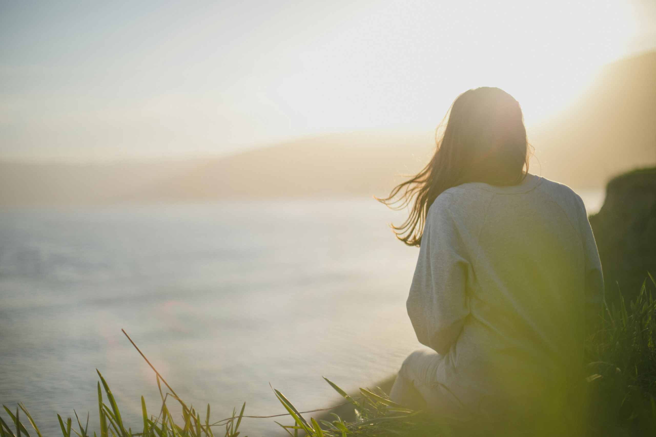 a person sitting on a hill looking at the ocean, how to embrace feminine energy